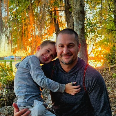 Brandon Kinsey holding a child outdoors at sunset.